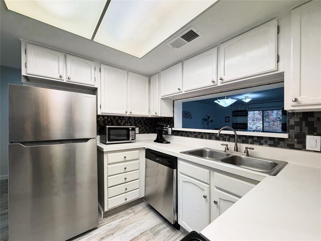 4565 North O'Connor Road, Unit 1304 Irving, TX 75062 - Photo 8 of 32 Kitchen featuring white cabinetry with silver hardware, stainless steel appliances, a dual basin sink with a high-arch faucet, a mosaic tile backsplash, and light-toned countertops