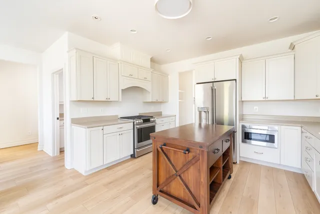 a kitchen with stainless steel appliances granite countertop a stove a sink dishwasher a refrigerator and white cabinets with wooden floor