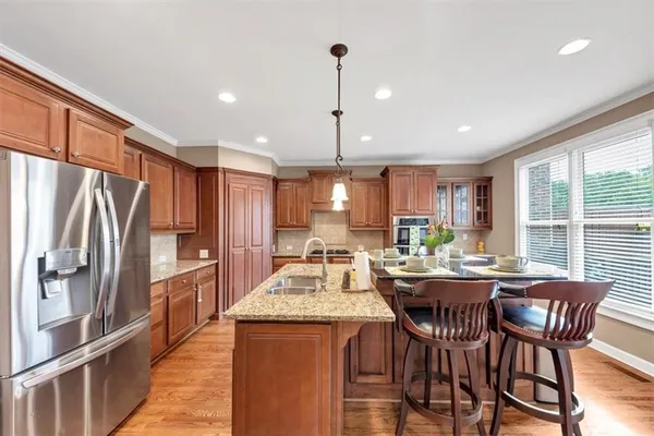 a kitchen with stainless steel appliances granite countertop a stove a refrigerator a kitchen island a dining table and chairs with wooden floor