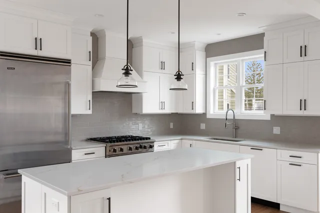 a kitchen with stainless steel appliances granite countertop a sink a stove a refrigerator and white cabinets