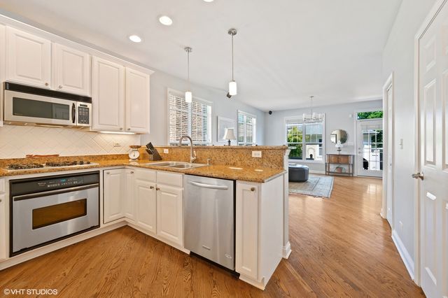 a kitchen with stainless steel appliances granite countertop a stove top oven a sink dishwasher and a refrigerator with wooden floor