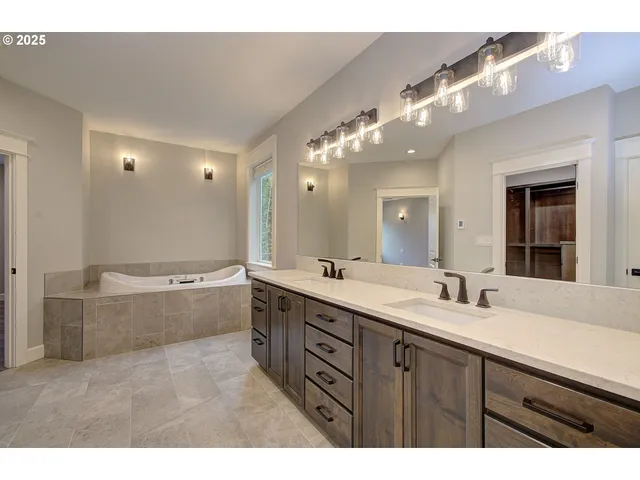a bathroom with a granite countertop double vanity sink a bathtub and mirror