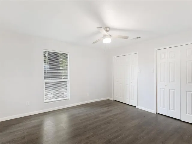 an empty room with wooden floor fan and windows