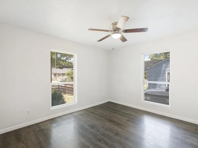 an empty room with wooden floor fan and windows