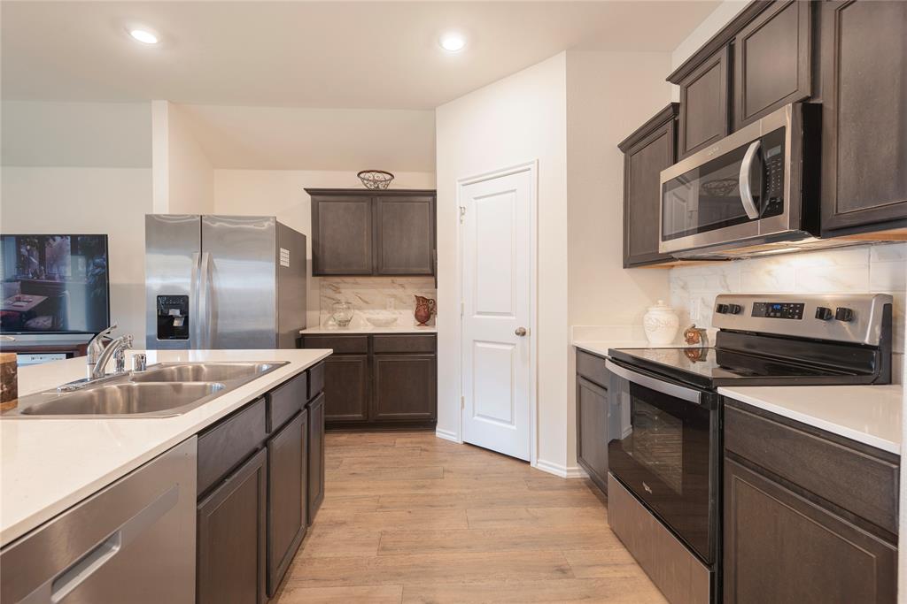 723 Primrose Lane Pilot Point, TX 76258 - Photo 22 of 37 Kitchen featuring stainless steel appliances, light wood-style flooring, tasteful ceramic backsplash, dark brown cabinets, and light countertops