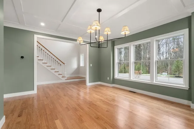 a view of an empty room with wooden floor kitchen view and a window