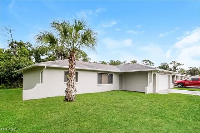 a palm tree sitting in front of a house with a garden