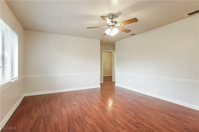 an empty room with wooden floor fan and windows