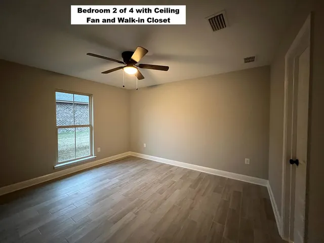 a view of an empty room with wooden floor and a ceiling fan