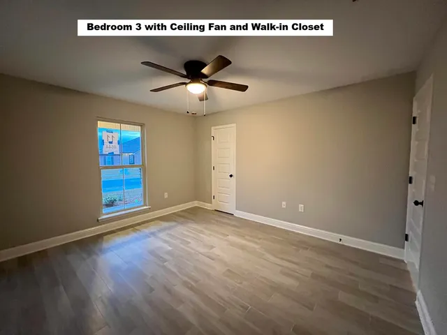 an empty room with wooden floor ceiling fan and windows