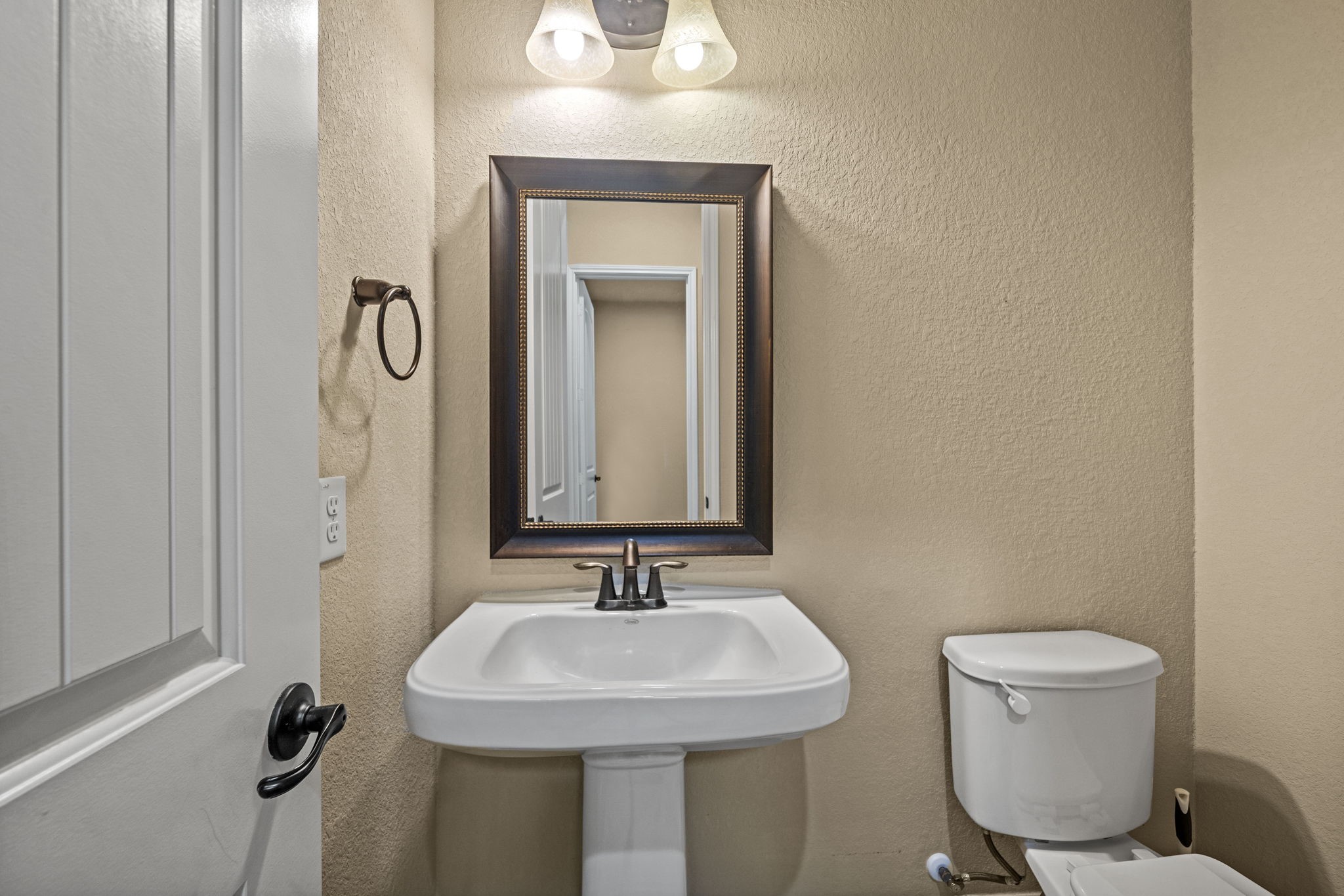 14215 Spindle Arbor Road Cypress, TX 77429 - Photo 36 of 47 This is a compact bathroom featuring a pedestal sink, toilet, and a framed mirror. The walls are painted in a neutral tone, and there is a light fixture above the mirror.