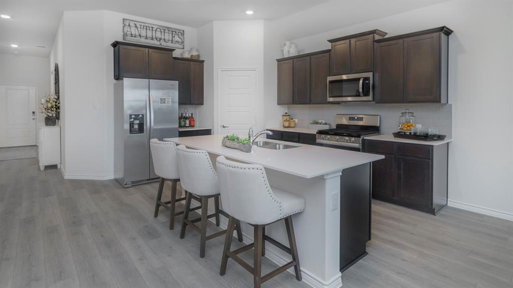 410 Range Road Caddo Mills, TX 75135 - Photo 9 of 19 Modern kitchen featuring an island with a breakfast bar, stainless steel appliances, dark wood-finish cabinetry, light countertops, and wood-look flooring