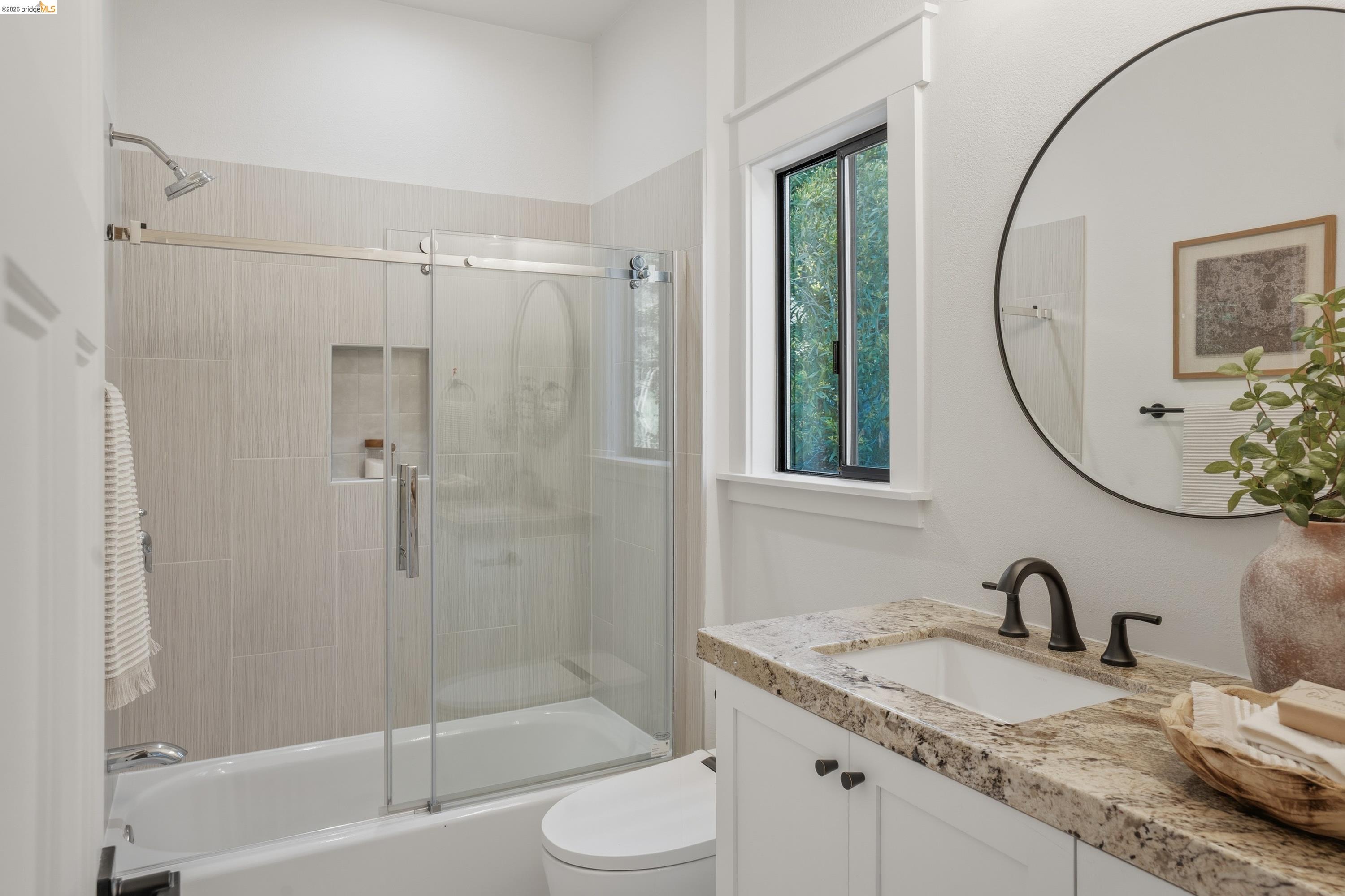 4120 Happy Valley Road Lafayette, CA 94549 - Photo 19 of 33 Bathroom featuring a white bathtub with a sliding glass door, a tiled shower surround with a built-in niche, a window with dark trim, a vanity with a light-colored countertop, and a round wall-mounted mirror