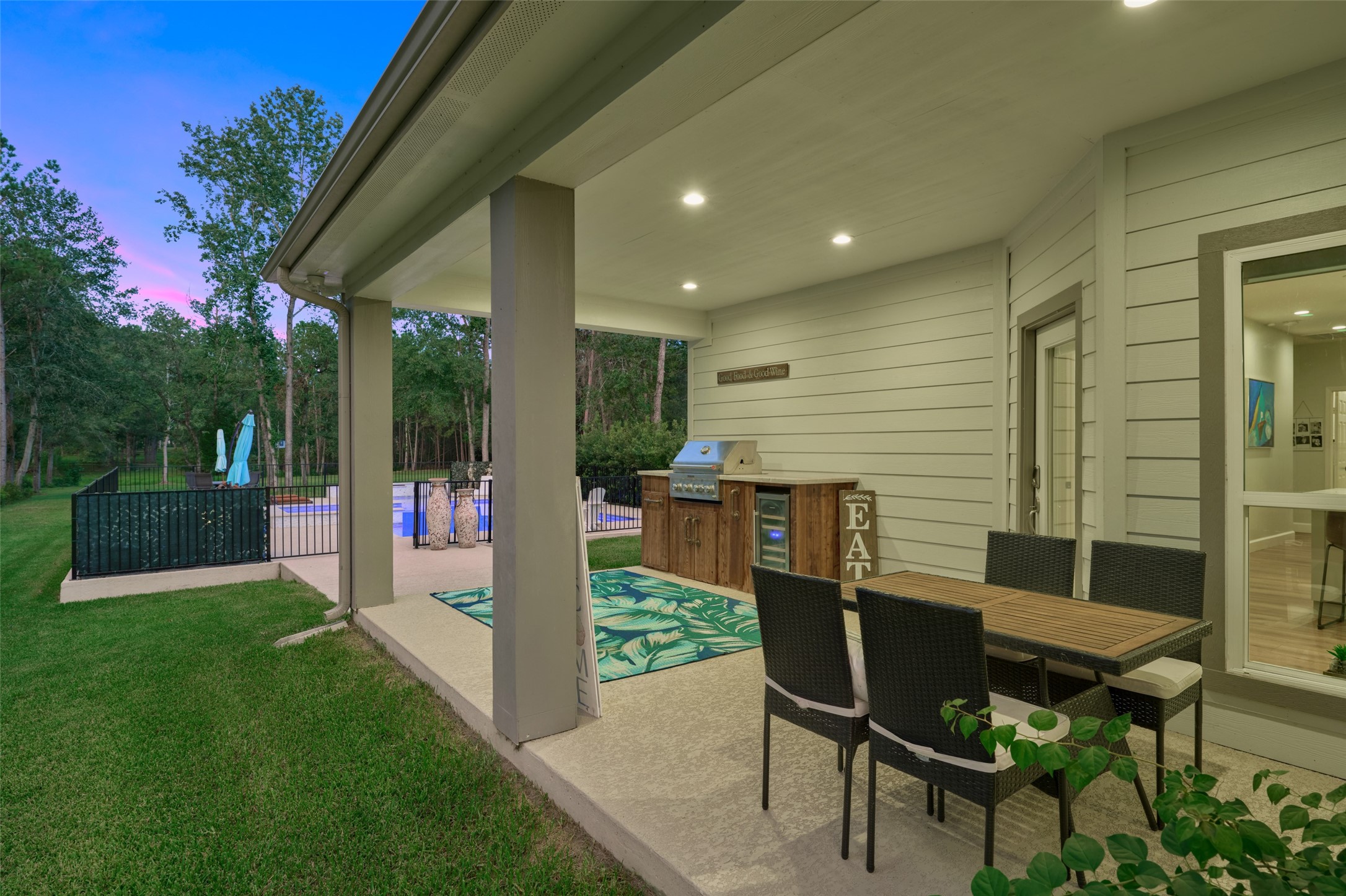 2218 Honea Egypt Road Magnolia, TX 77354 - Photo 20 of 50 This photo showcases a spacious covered patio with outdoor dining furniture, providing a seamless transition to a fenced-in pool area set against a backdrop of lush greenery for privacy and relaxation.