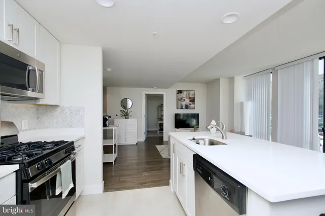 a kitchen with stainless steel appliances a refrigerator a stove a dining table and chairs with wooden floor