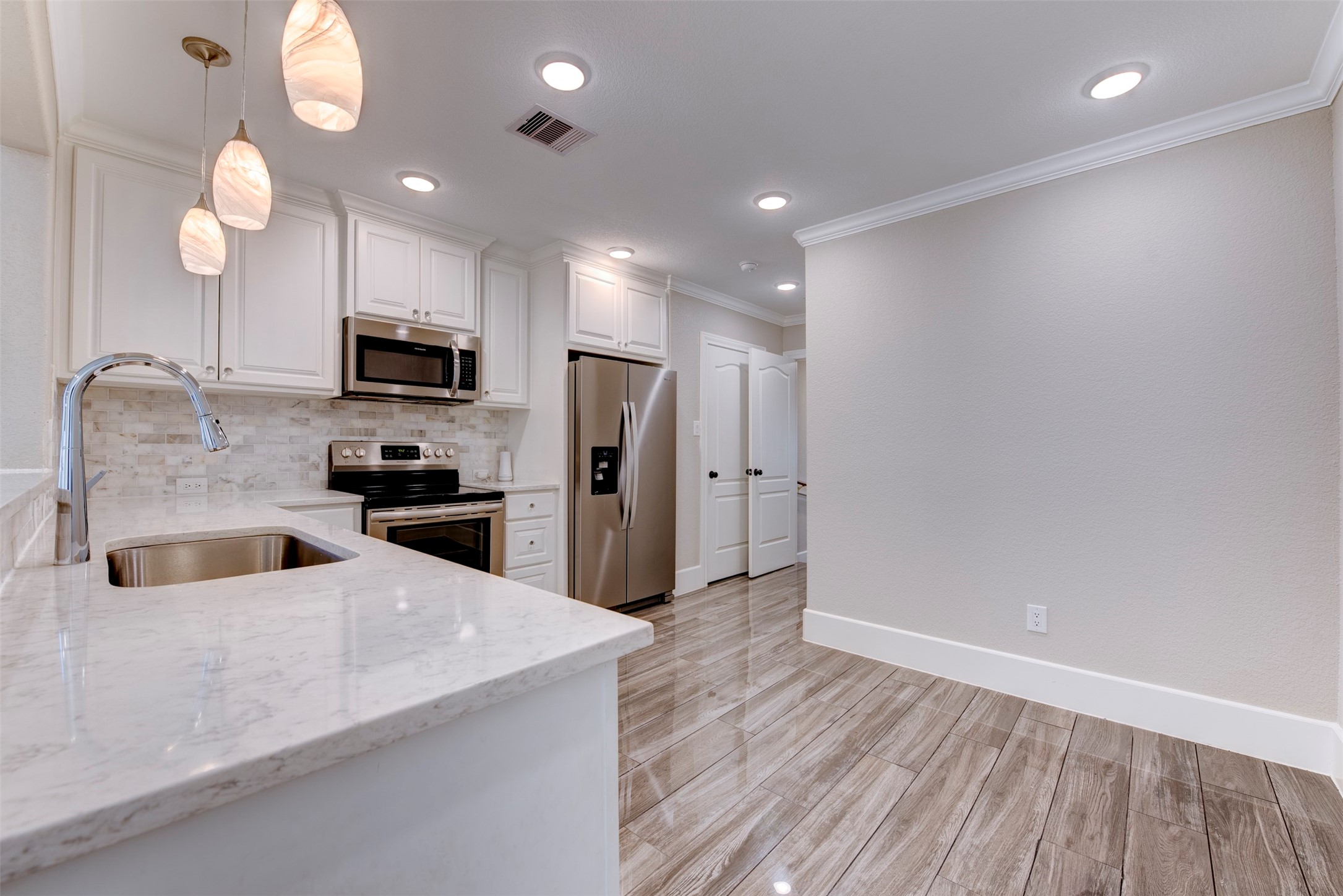 109 Dresden Street Houston, TX 77012 - Photo 14 of 43 Modern kitchen with white cabinetry, stainless steel appliances, and a marble countertop. Warm pendant lighting and wood-look tile flooring add a cozy touch.