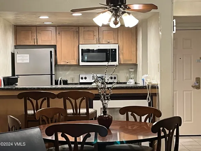 a kitchen with stainless steel appliances granite countertop a dining table chairs refrigerator and microwave