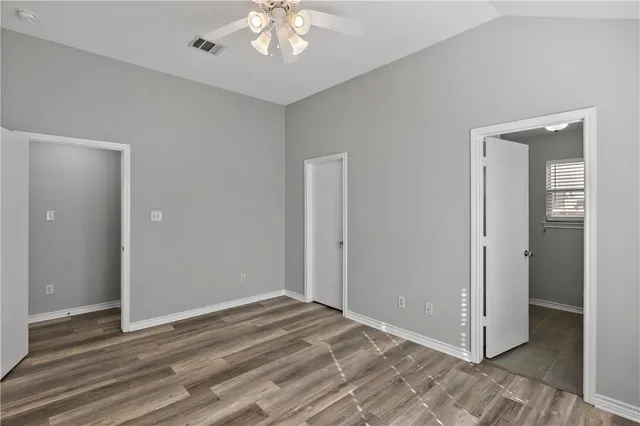 an empty room with wooden floor and way to kitchen