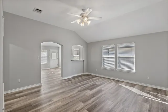 an empty room with wooden floor chandelier fan and windows