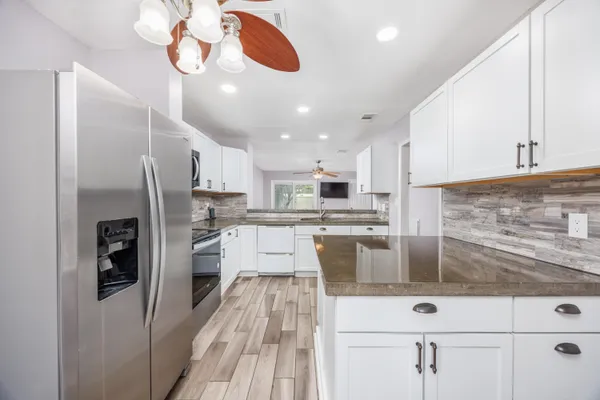 a large kitchen with stainless steel appliances kitchen island granite countertop a refrigerator a stove a sink and white cabinets with wooden floor