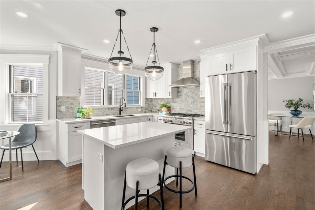 11 Macarthur Street, Unit A Somerville, MA 02145 - Photo 8 of 35 a kitchen with stainless steel appliances granite countertop a refrigerator a sink dishwasher a stove and a dining table with wooden floor