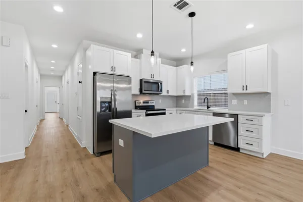 a kitchen with stainless steel appliances white cabinets a sink a stove a refrigerator and a center island