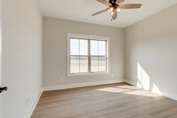 an empty room with wooden floor fan and windows