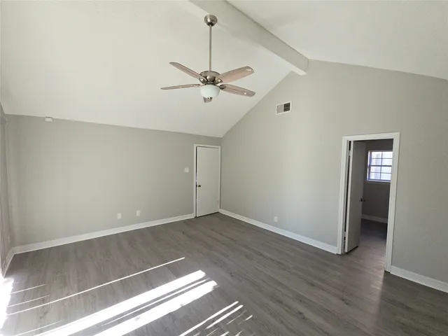 a view of an empty room with wooden floor and a ceiling fan