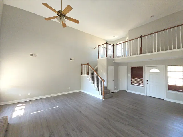 a view of an empty room with wooden floor and a ceiling fan