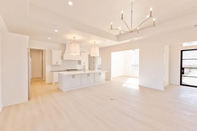 a large white kitchen with kitchen island a stove a sink a refrigerator and white cabinets with wooden floor