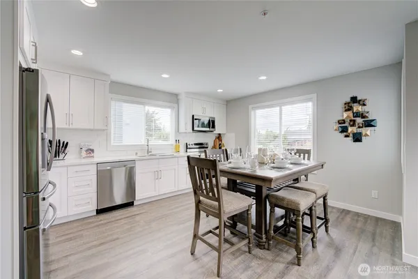 a kitchen with stainless steel appliances kitchen island granite countertop a stove a sink a microwave a refrigerator and white cabinets with wooden floor