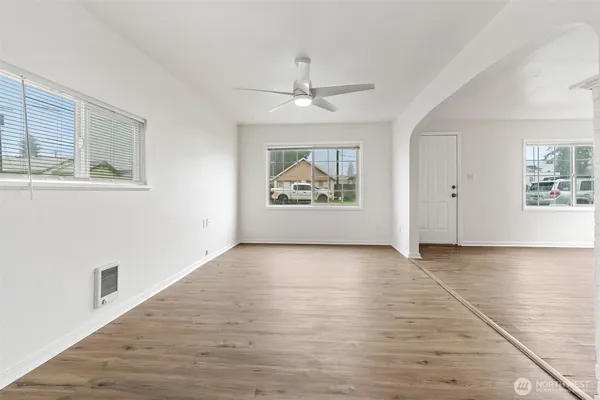 an empty room with wooden floor chandelier fan and windows
