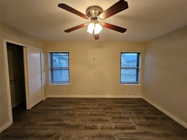 an empty room with a chandelier fan and wooden floor
