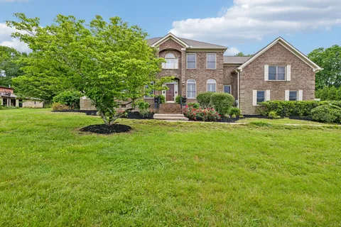 a view of a brick house with a big yard and large trees