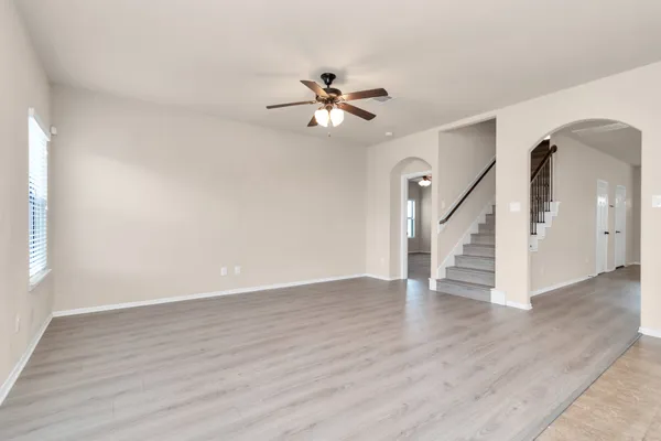 a view of an empty room with wooden floor and a ceiling fan