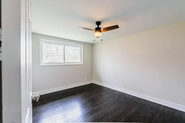 an empty room with wooden floor ceiling fan and windows