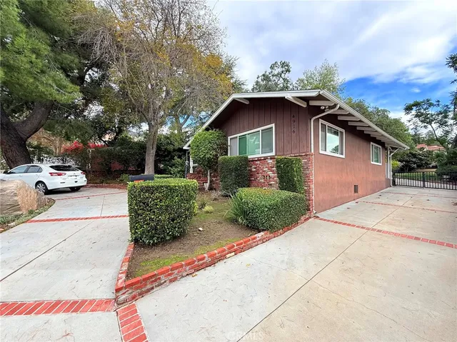 a view of a house with a yard plants and a large tree