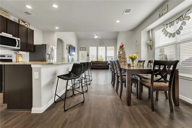 a kitchen with stainless steel appliances granite countertop a dining table chairs stove refrigerator and cabinets