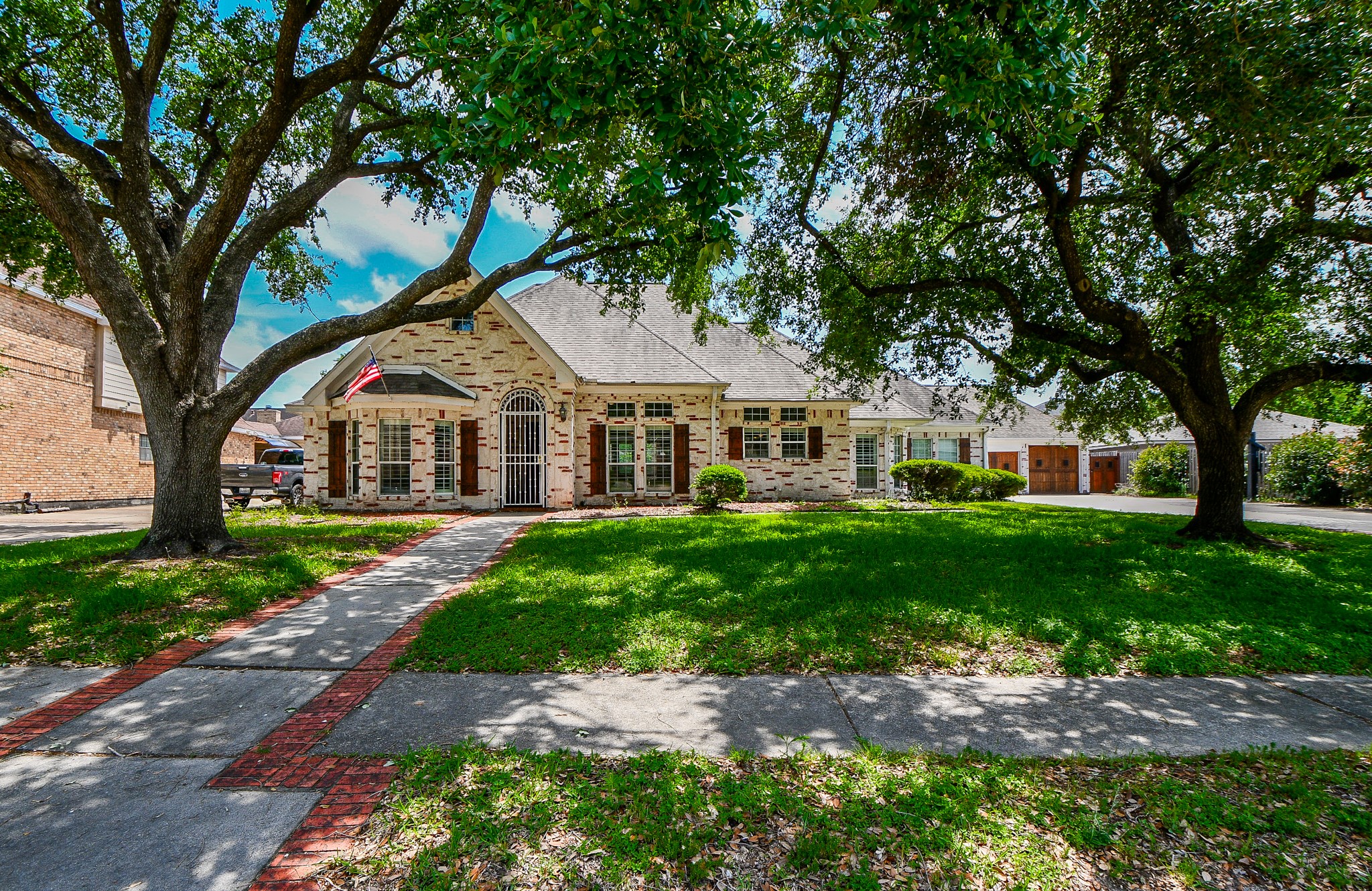 263 Wood Loop Street Houston, TX 77015 - Photo 2 of 45 Charming single-story home with a brick exterior, nestled under mature trees. Features a welcoming front path, manicured lawn, and a classic American flag. Ideal for those seeking a serene neighborhood setting.