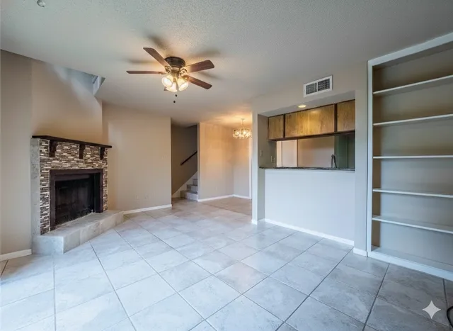 a view of an empty room with a fireplace and a chandelier fan