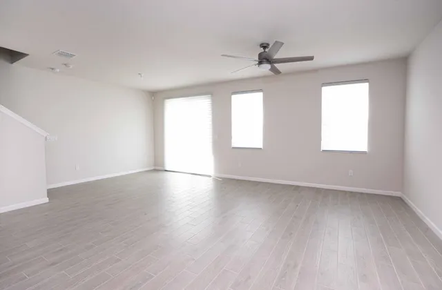 an empty room with wooden floor ceiling fan and windows