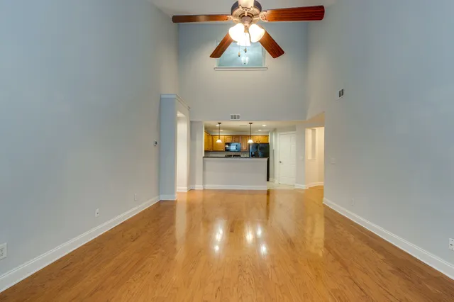 an empty room with wooden floor chandelier fan and windows