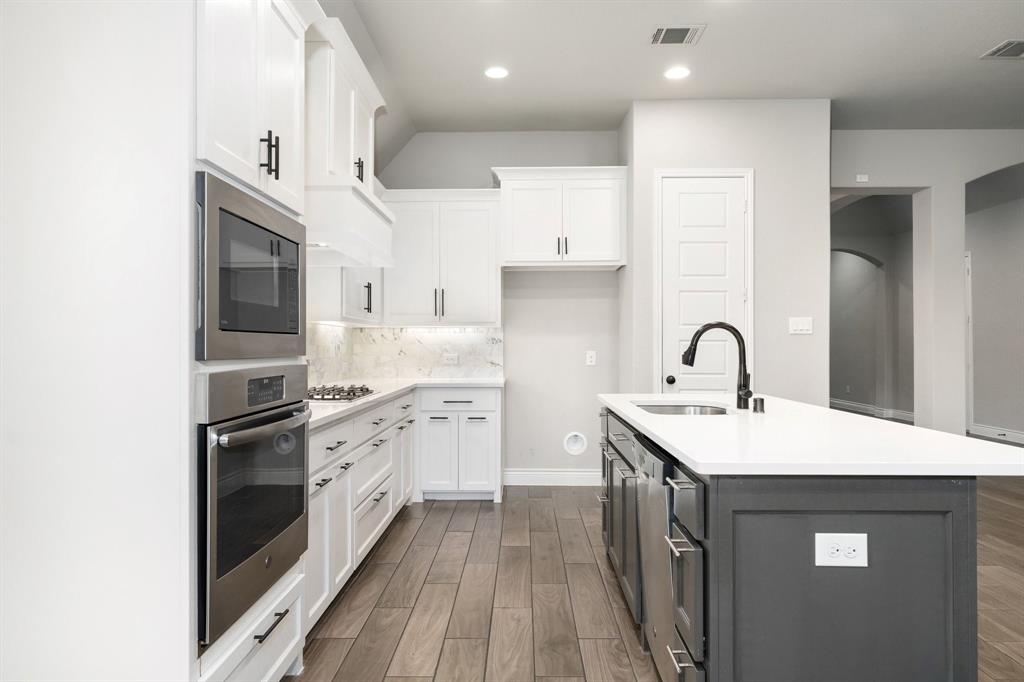 1501 Calcot Lane Forney, TX 75126 - Photo 14 of 34 Gourmet kitchen featuring white cabinetry, stainless steel appliances, a white countertop island with an undermount sink, a gas cooktop with a marble-patterned backsplash, and wood-finish flooring