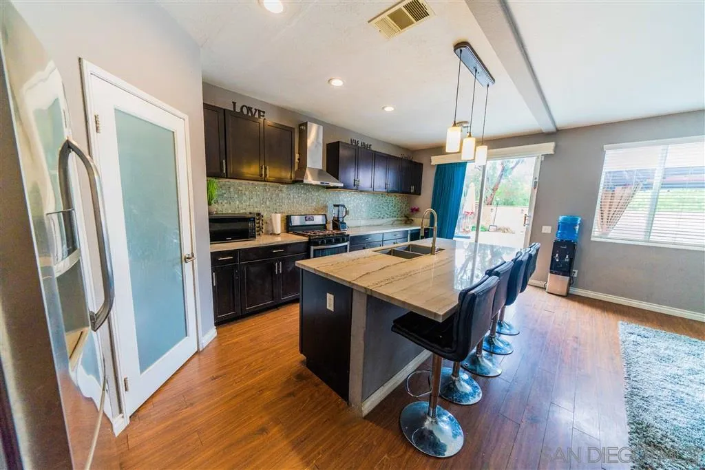 38917 Rockinghorse Road Murrieta, CA 92563 - Photo 3 of 22 a kitchen with stainless steel appliances granite countertop a refrigerator a sink dishwasher a stove and a dining table with wooden floor