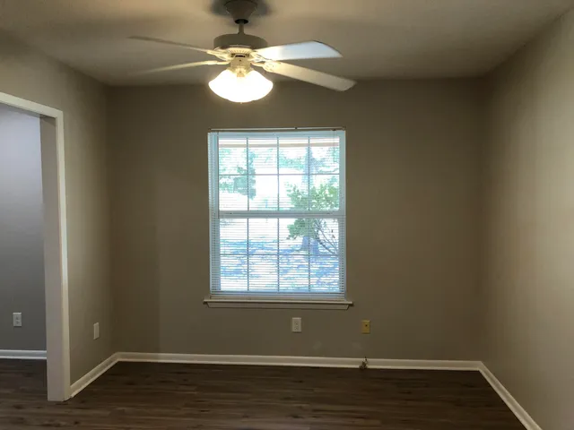 an empty room with wooden floor chandelier fan and windows