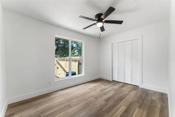 an empty room with wooden floor chandelier fan and windows