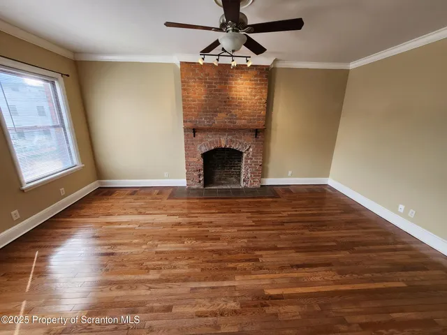 a view of an empty room with wooden floor fireplace and a window