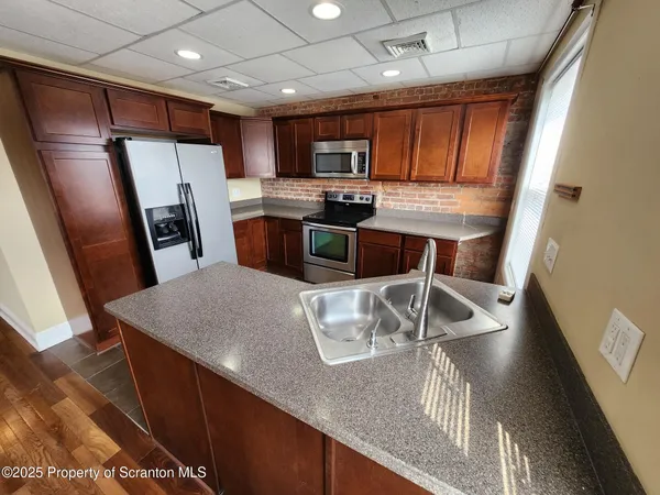 a kitchen with stainless steel appliances granite countertop a refrigerator a stove a sink a microwave oven with white cabinets and wooden floor
