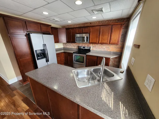 a kitchen with stainless steel appliances granite countertop a refrigerator a stove a sink a microwave oven with white cabinets and wooden floor