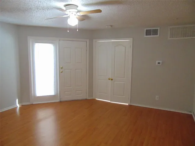 an empty room with wooden floor fan and windows